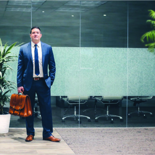 Attorney standing outside of a conference room in a blue suit holding a brown briefcase