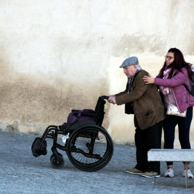 Person assisting a man who uses a wheelchair Person assisting a man who uses a wheelchair